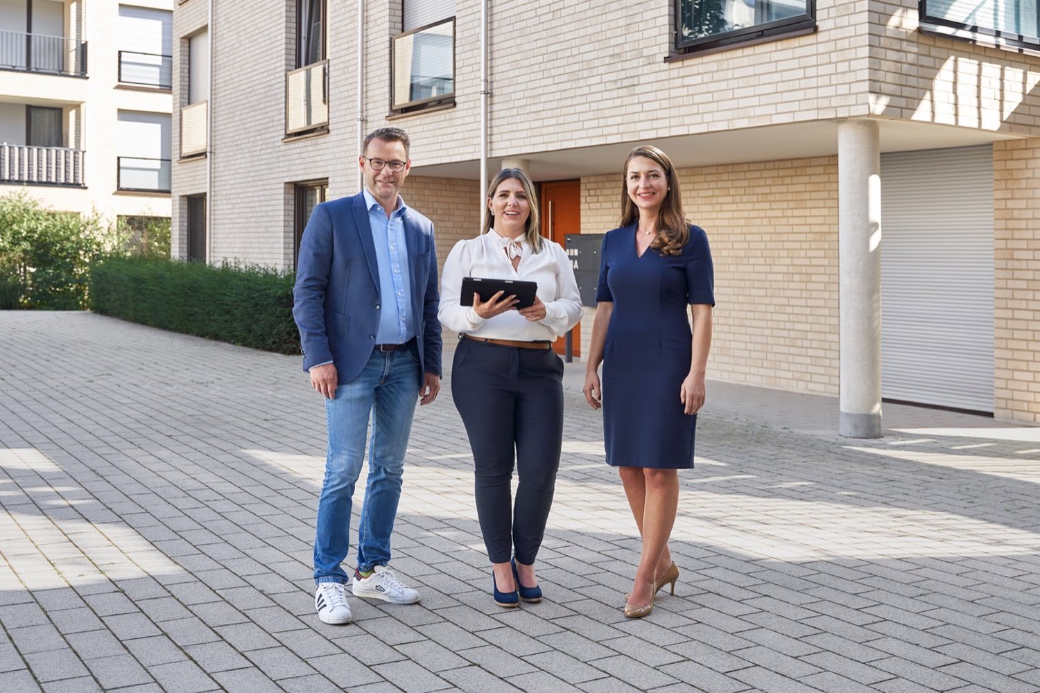Drei Personen stehen vor einem Gebäude und schauen in die Kamera