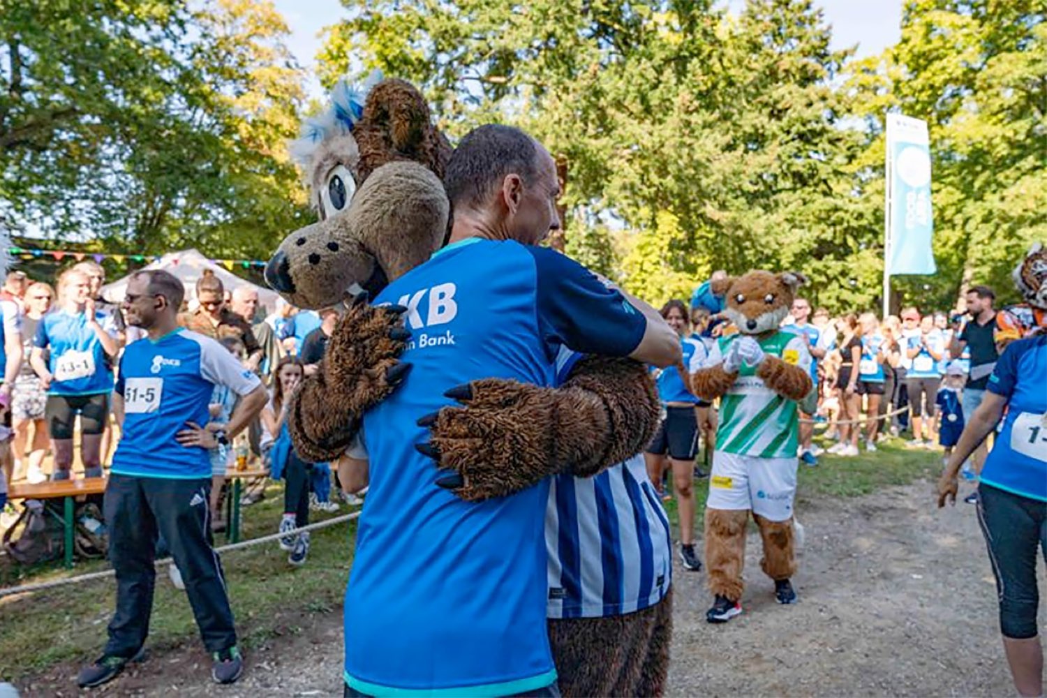 Mitarbeiter und das DKB Maskottchen umarmen sich