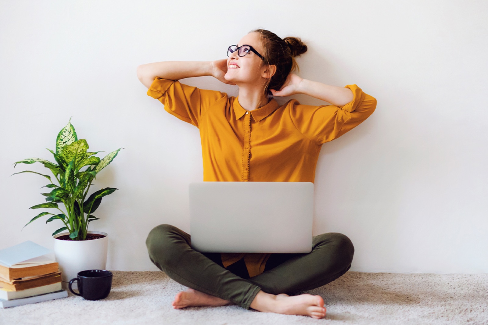 Eine gut gelaunt wirkende Frau sitzt auf dem Boden und hat ihren Laptop auf dem Schoß