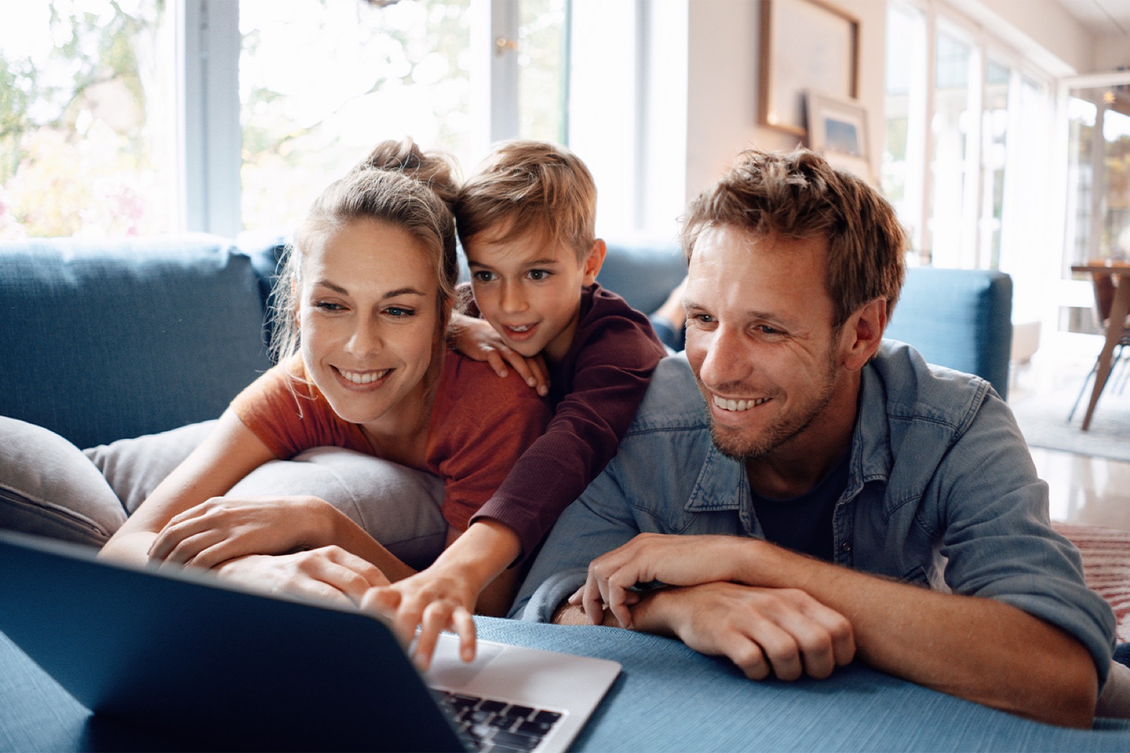 Eine Frau, ein Mann und ein Kind sitzen vor einer Couch und shoppen an einem Laptop online