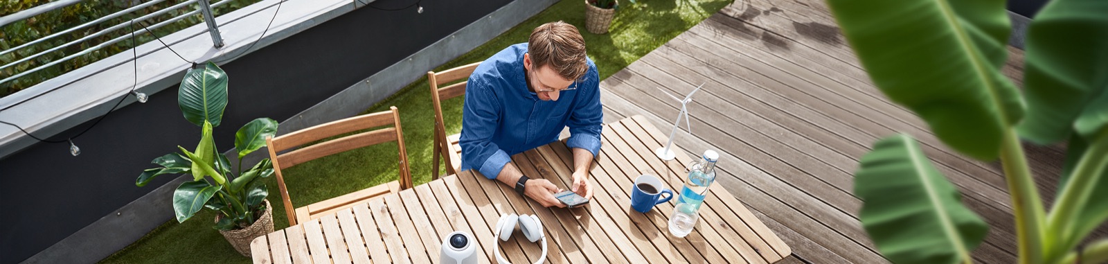 Ein Mann sitzt mit Smartphone in der Hand auf einer Terrasse
