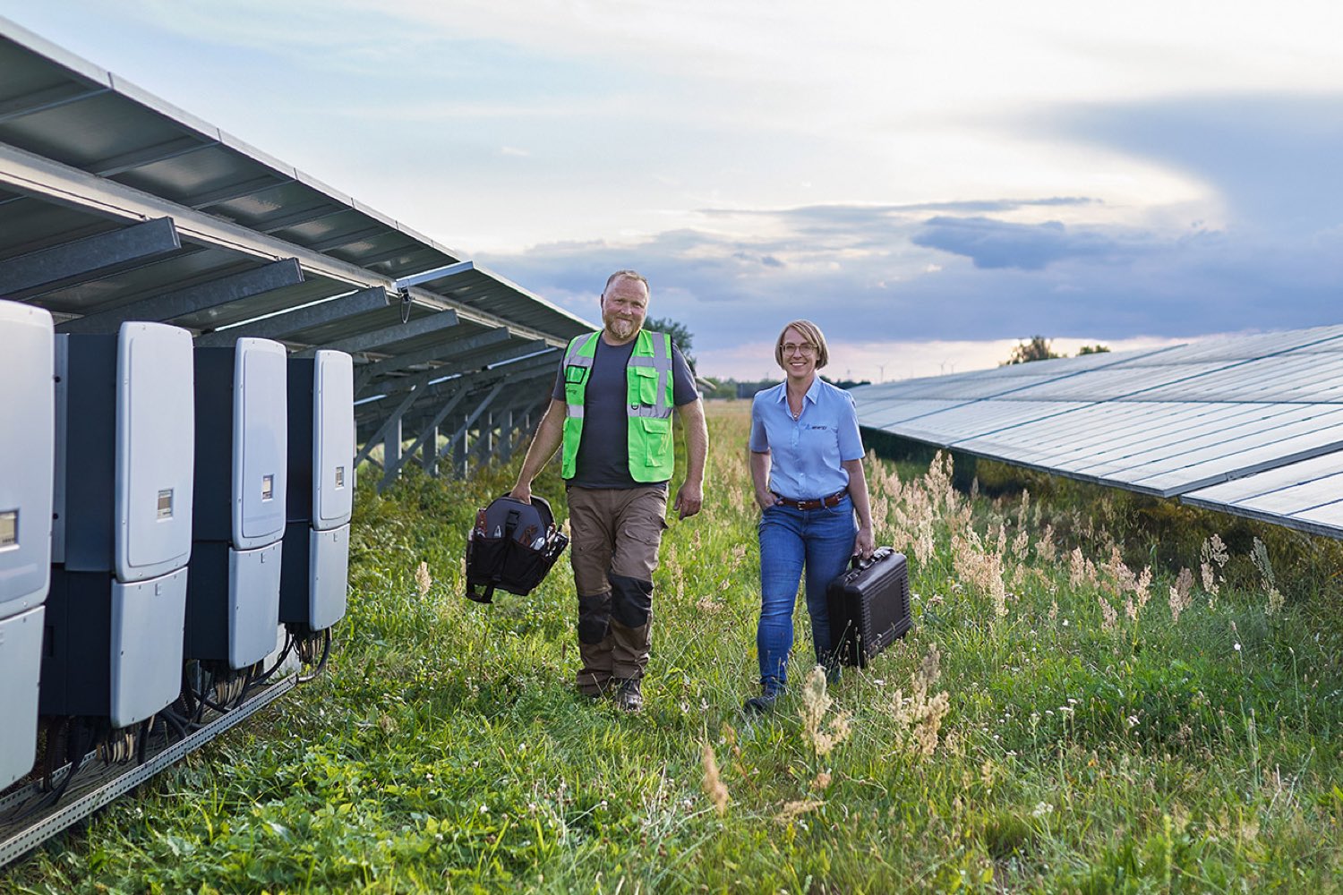Personen laufen auf einem Feld in Niedergörsdorf an Wechselrichtern einer Solaranlage vorbei
